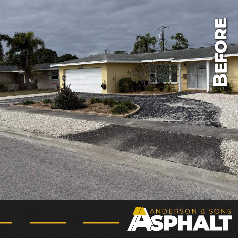 Faded, worn asphalt on a circular driveway and street apron in front of a yellow house, before resealing