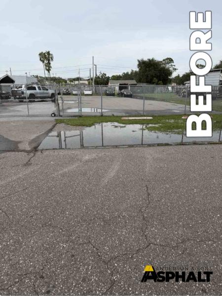 Grassy strip holding standing water next to a cracked asphalt lot, before paving