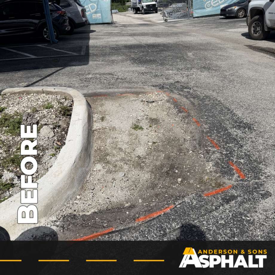 Failed asphalt removed down to the base at the end of a curbed island, with repair edges marked in orange paint