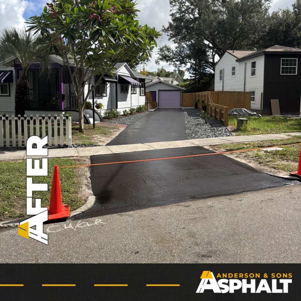 Freshly sealcoated black asphalt driveway apron with a safety cone and caution line