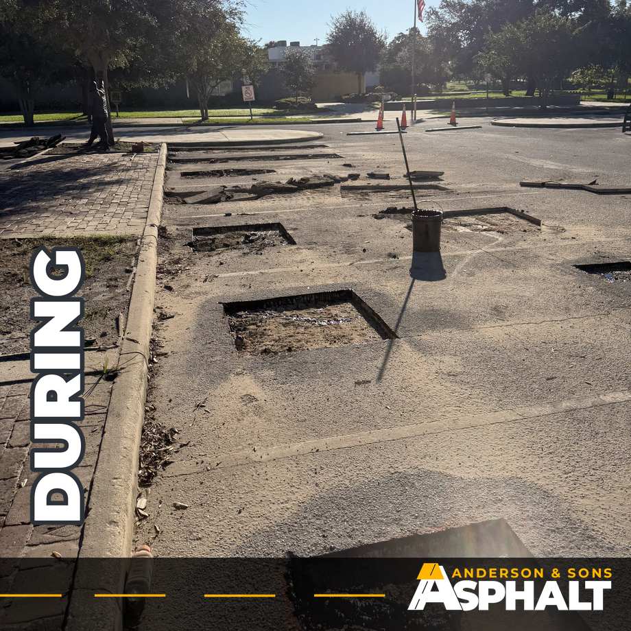 Several asphalt sections removed down to the base in parking stalls beside a curbed island