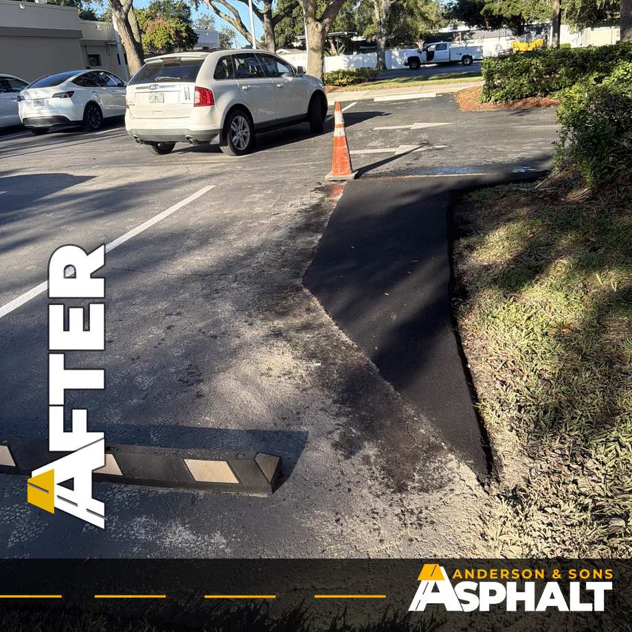 New asphalt edge repair along a parking lot island with a traffic cone and wheel stop